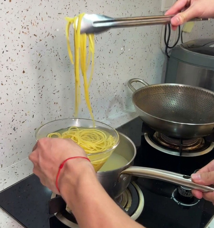 Szczypce kuchenne wyjmujące ugotowane spaghetti z gorącej wody i przekładające je do miski z zimną wodą.