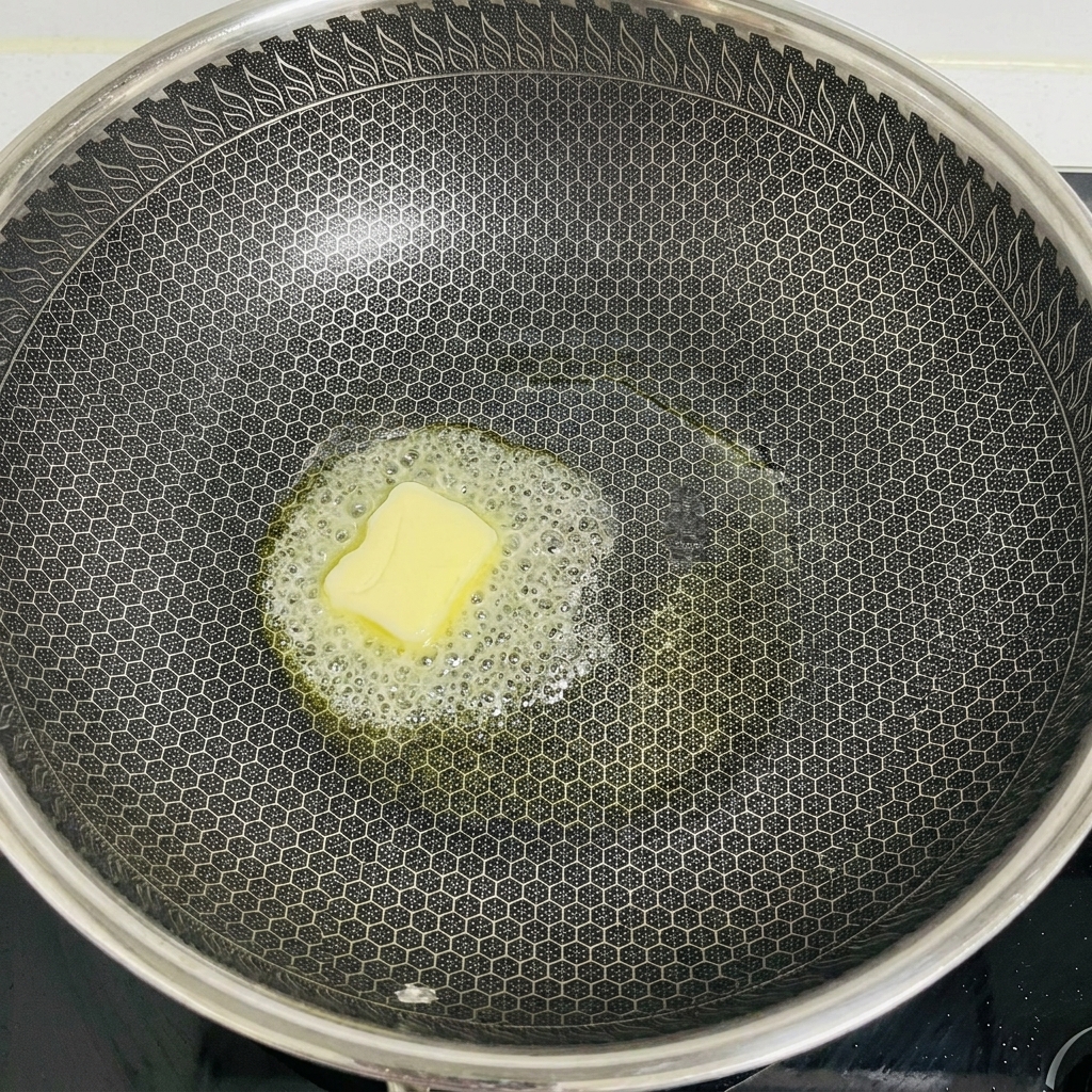 Kostka masła roztapiająca się i pieniąca na środku dużej patelni typu wok.