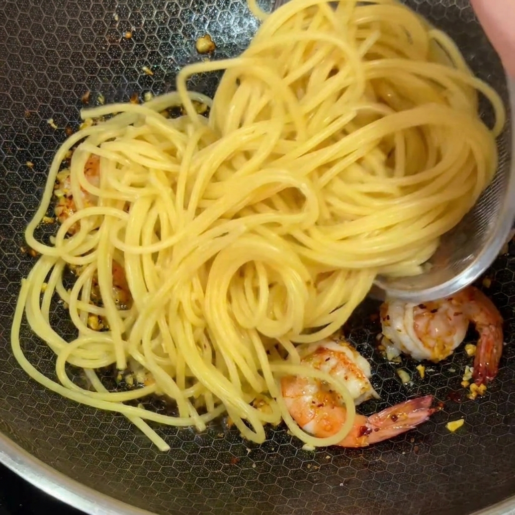 Ugotowany makaron spaghetti dodawany do woka z krewetkami i czosnkiem.