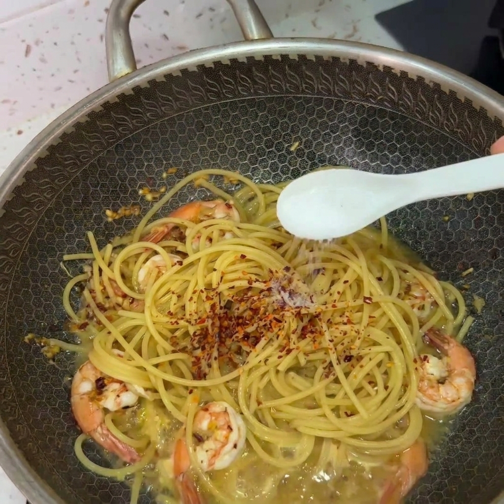Biała łyżeczka posypująca solą spaghetti z krewetkami i chili w woku.