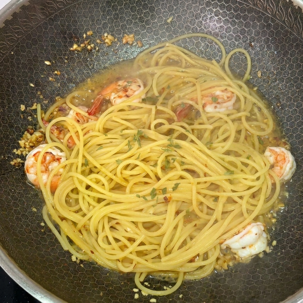 Spaghetti z krewetkami w woku posypywane świeżą zieloną pietruszką.