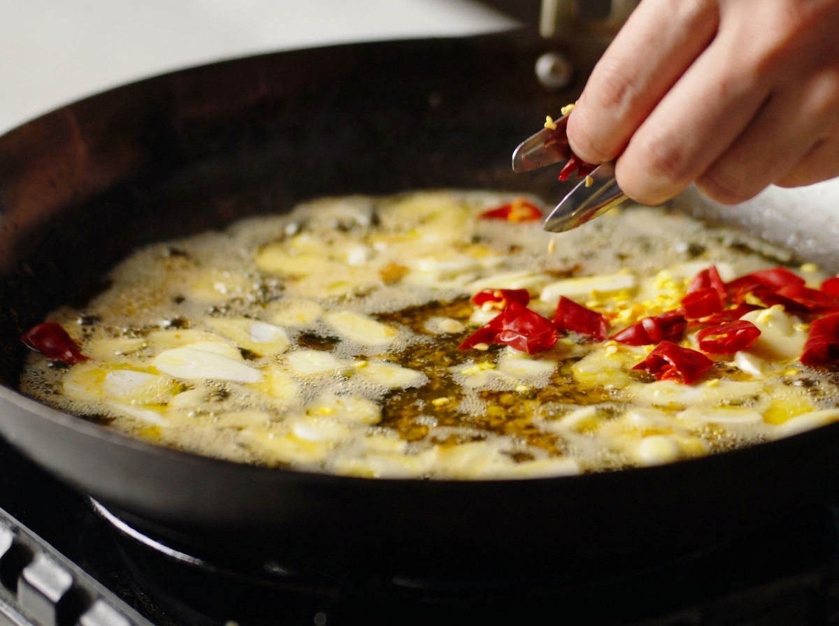 Dłoń wrzucająca kawałki suszonego chili do woka z czosnkiem.