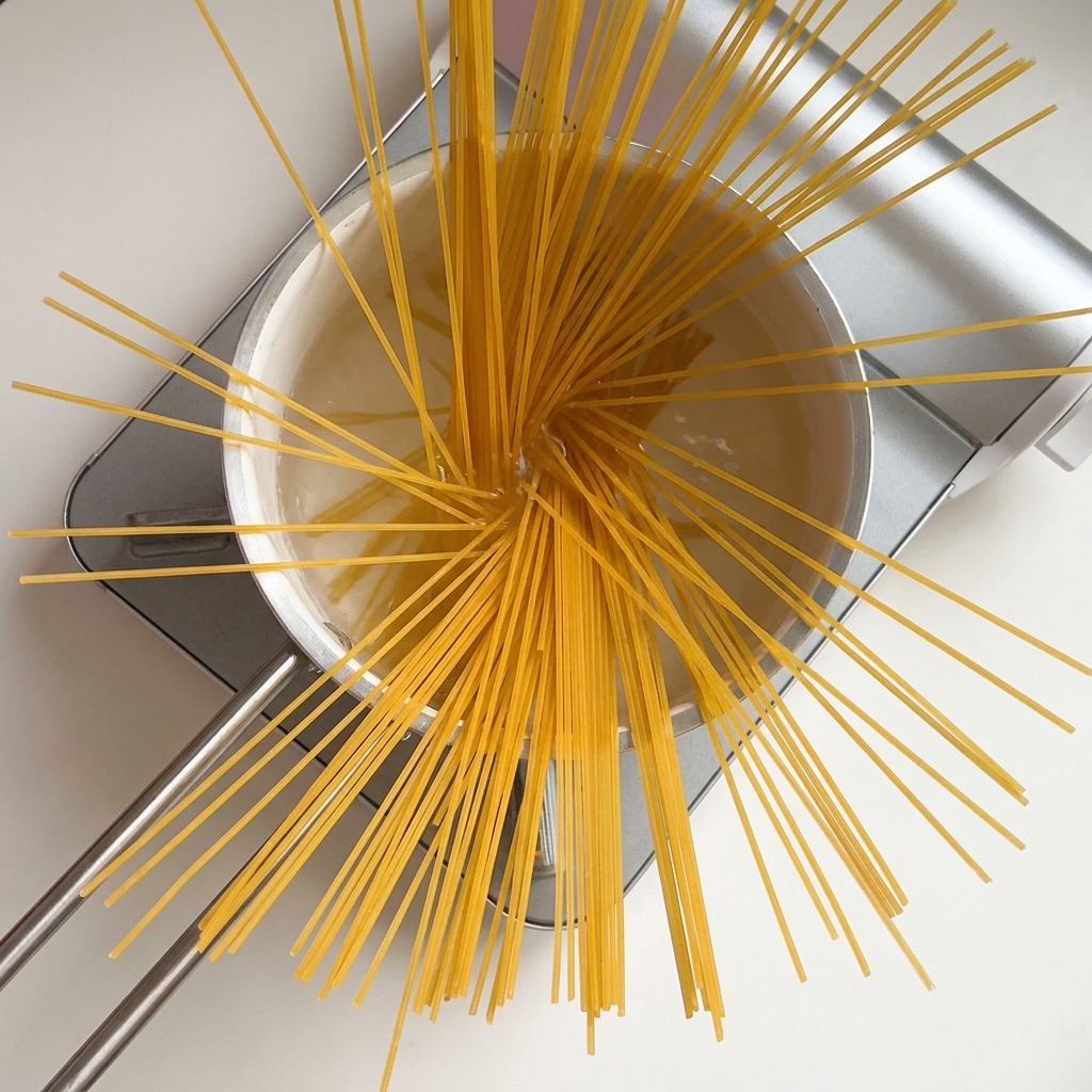 Suchy makaron spaghetti rozłożony wachlarzowato w garnku z wrzącą wodą.