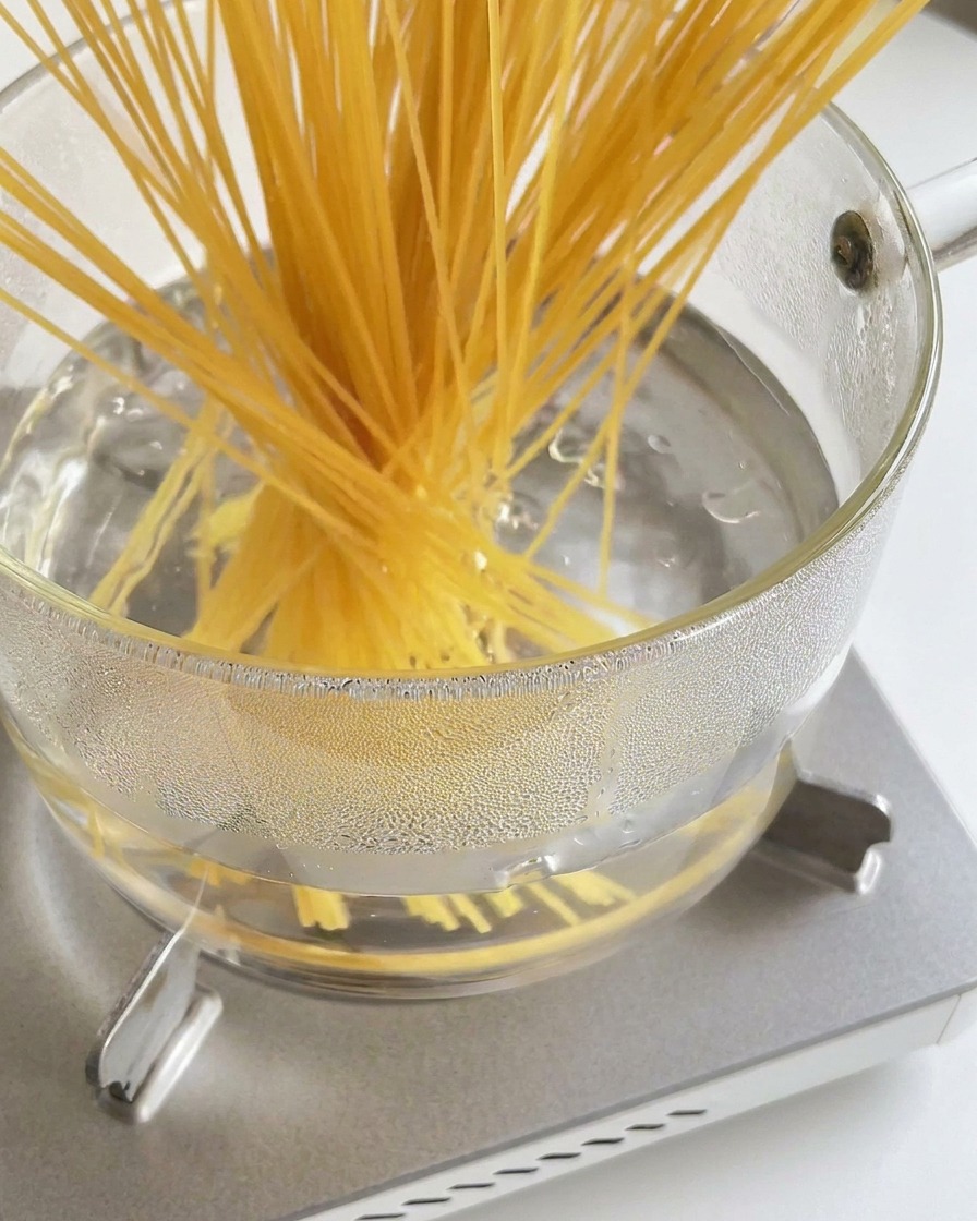 Wiązka suchego makaronu spaghetti wkładana do garnka z wrzącą wodą.