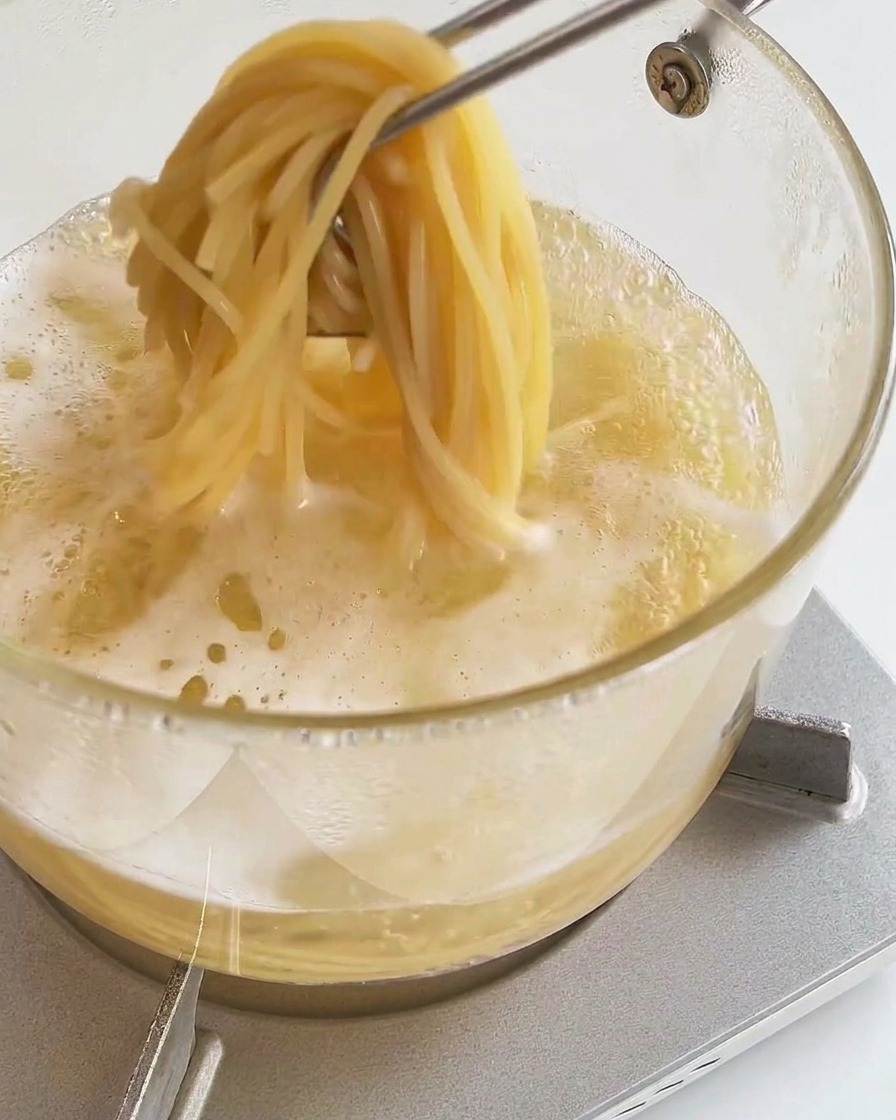 Szczypce kuchenne wyciągające porcję miękkiego spaghetti z garnka z wrzątkiem.