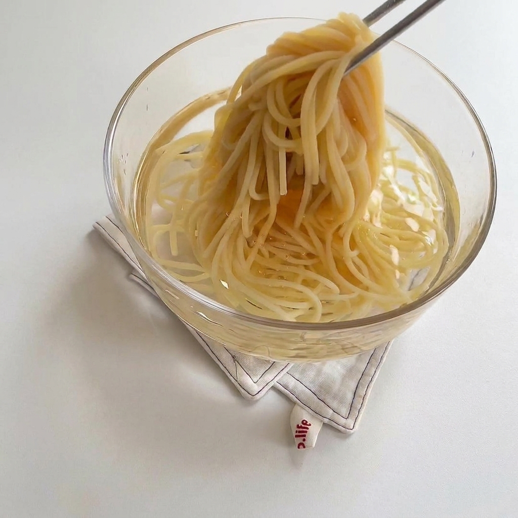 Ugotowany makaron spaghetti przekładany do szklanej miski z zimną wodą.