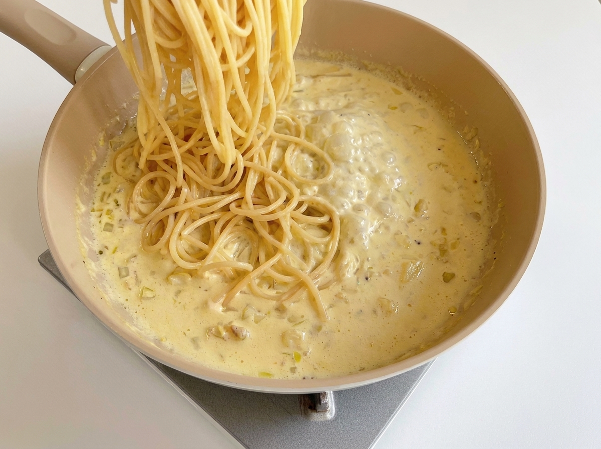 Ugotowany makaron spaghetti wkładany na patelnię z gotowym sosem serowym.