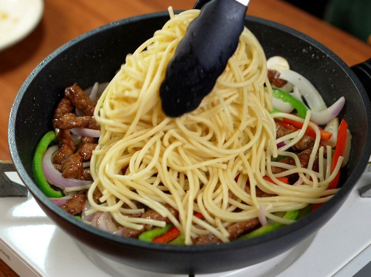 Szczypce nakładające ugotowane spaghetti na patelnię z wołowiną i warzywami.