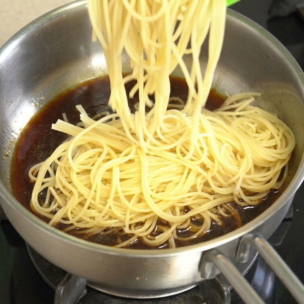 Ugotowane spaghetti dodawane na patelnię wypełnioną ciemnobrązowym sosem pieprzowym.