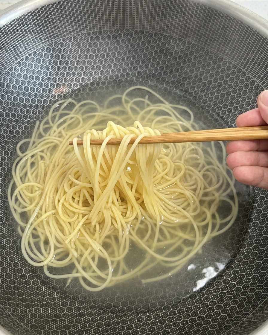 Ugotowany makaron spaghetti wyjmowany z gorącej wody za pomocą drewnianych pałeczek.