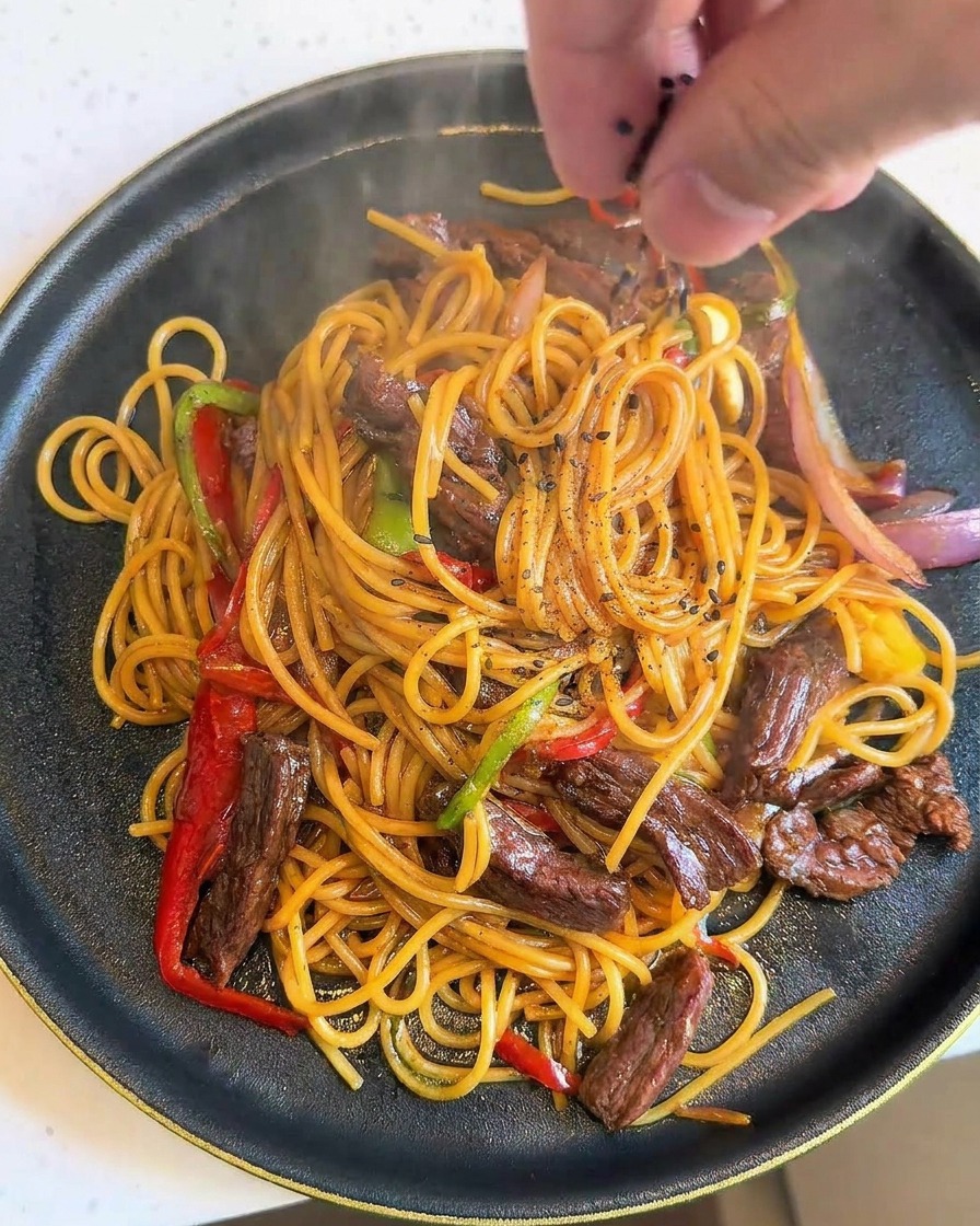 Dłoń posypująca czarnym sezamem świeżo nałożone, parujące spaghetti z wołowiną.