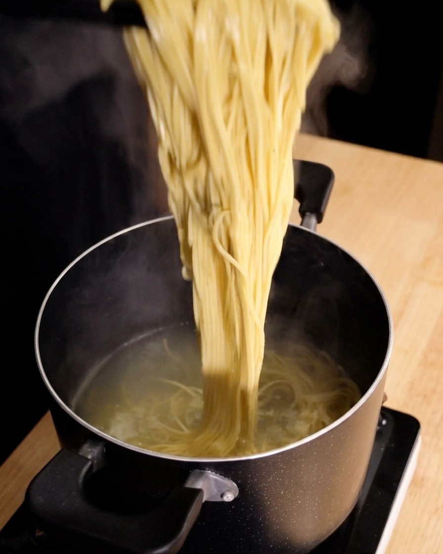 Szczypce kuchenne wyjmujące parujące spaghetti prosto z garnka z wrzącą wodą.