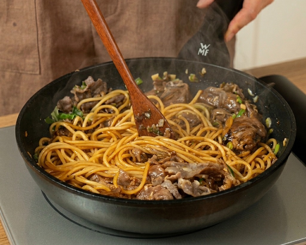 Mieszanie spaghetti, wołowiny i ciemnego sosu drewnianą łopatką na patelni.