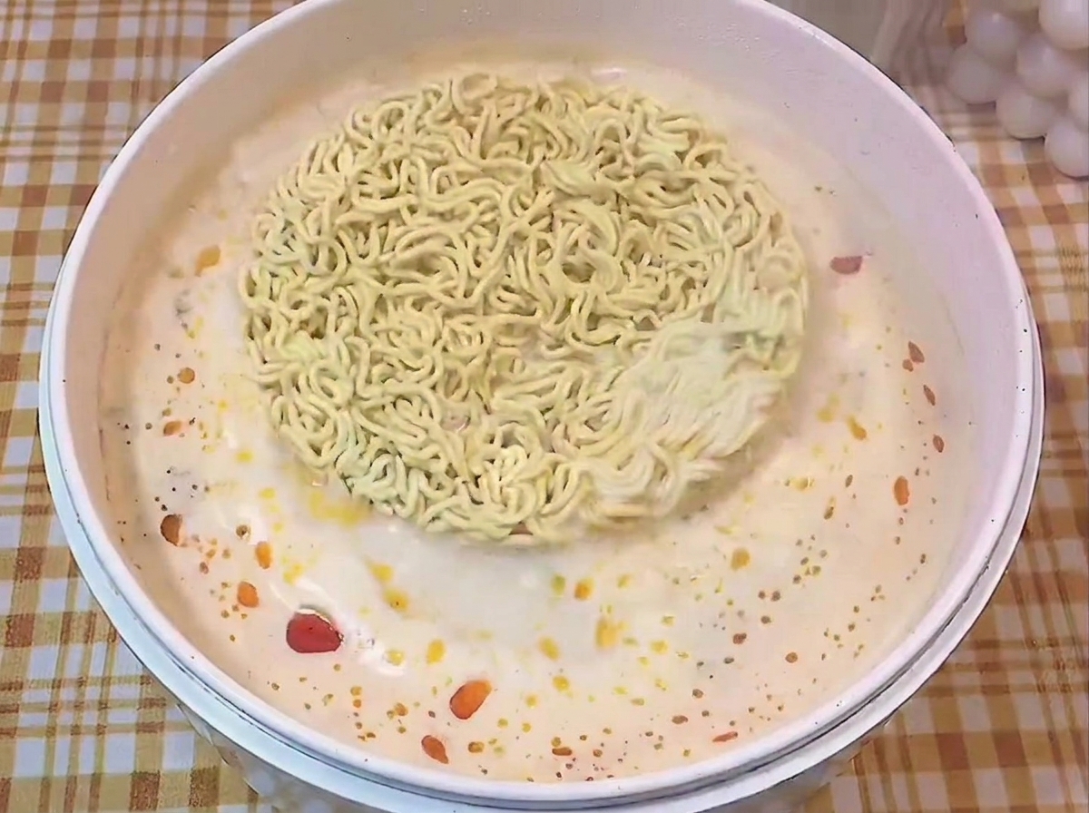 Blok makaronu ramen pływający w białym garnku z przyprawionym wywarem.