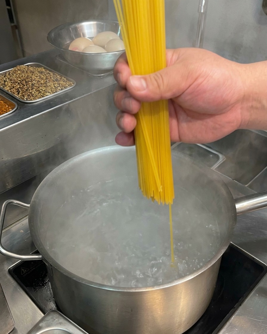 Wkładanie suchego makaronu spaghetti do garnka z wrzącą wodą.