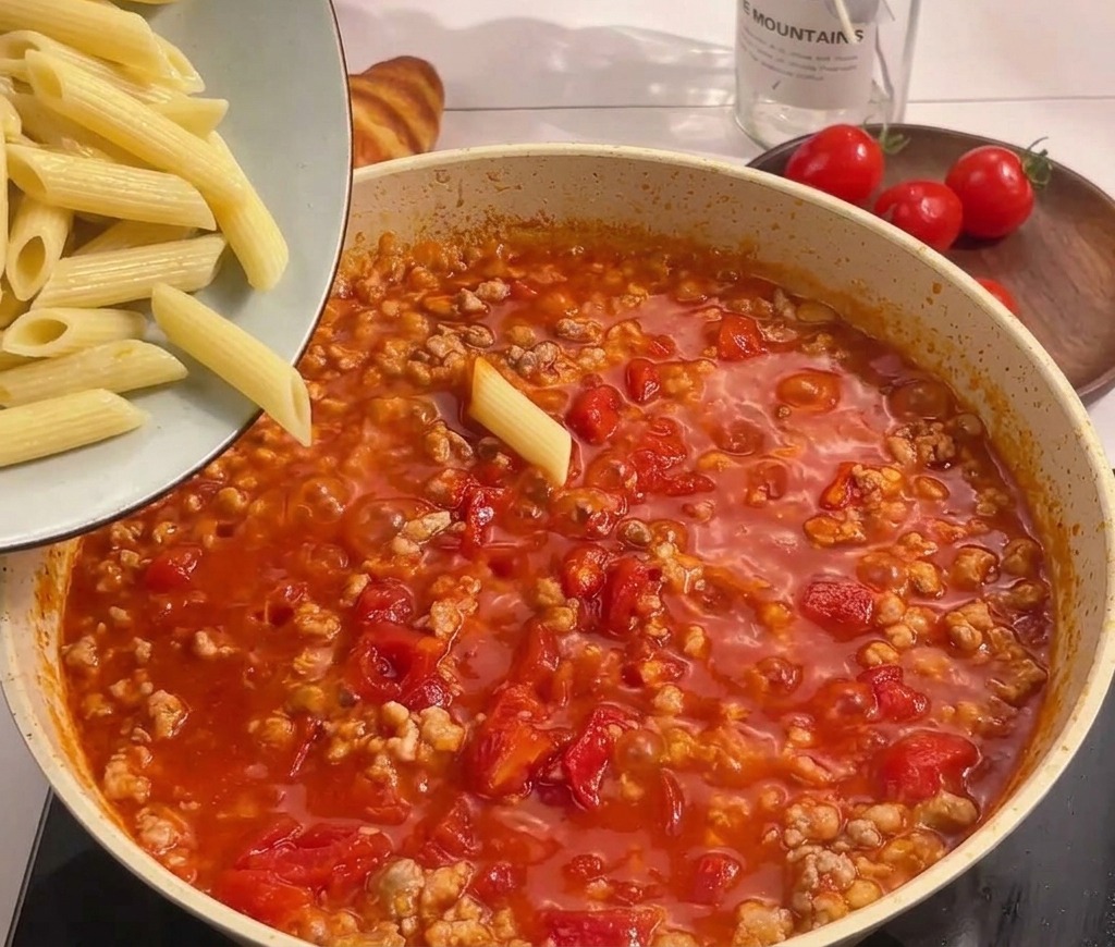 Ugotowany makaron penne przesypywany z miski do gotującego się sosu.
