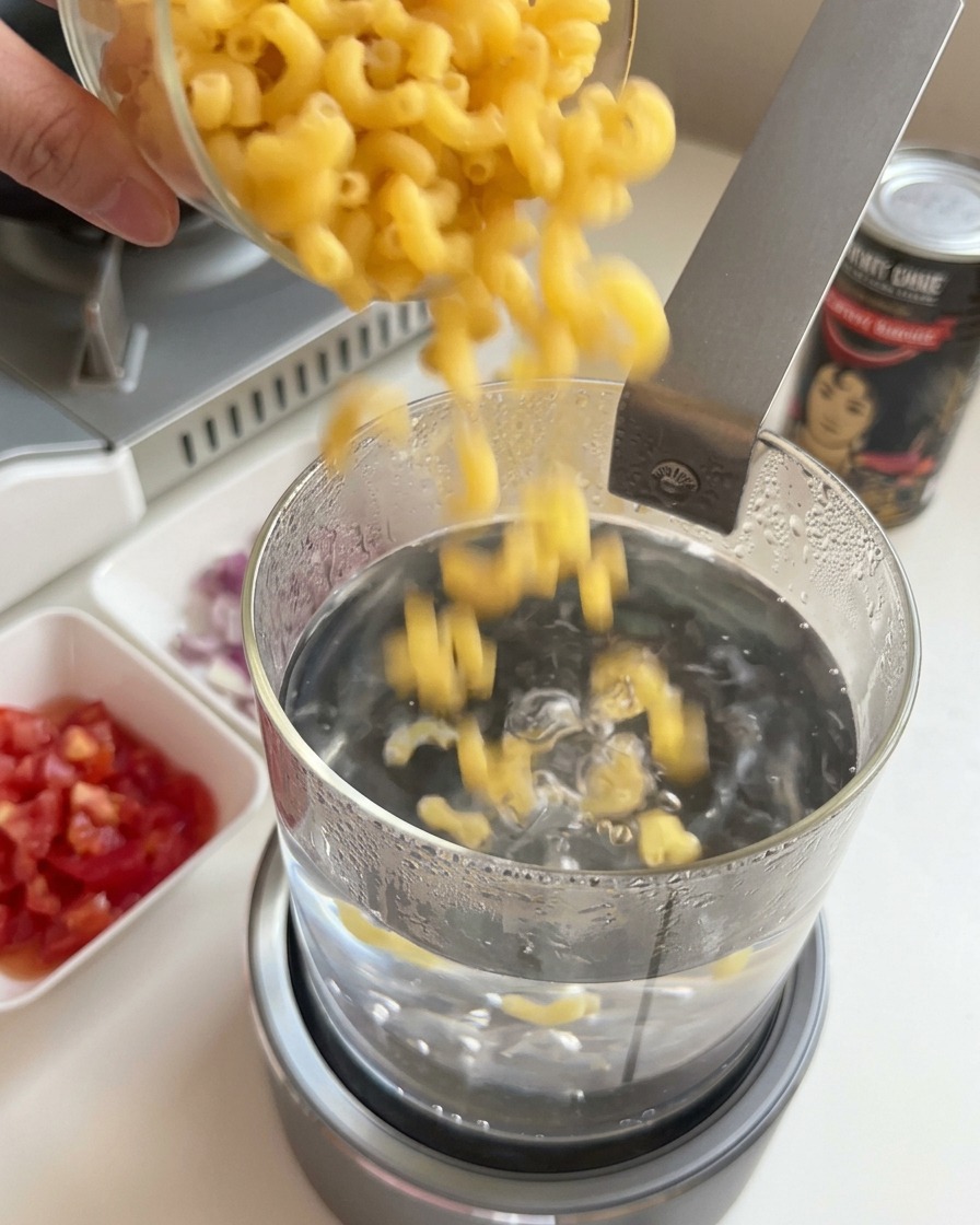 Wsypywanie suchego makaronu kolanka do szklanego garnka z wrzącą wodą.