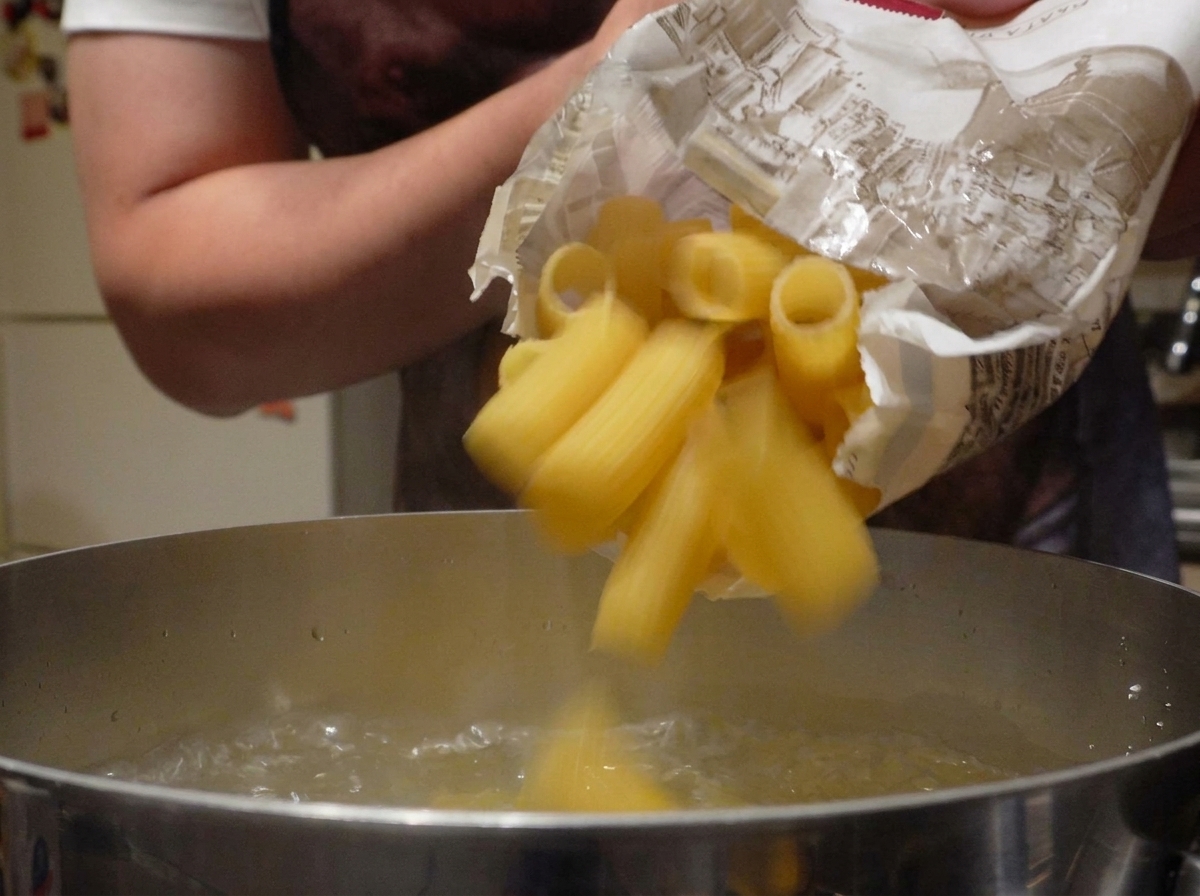 Suchy makaron rigatoni wsypywany do garnka z wrzącą wodą.