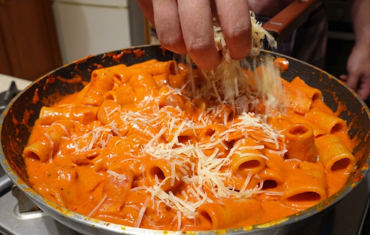 Starty parmezan sypany dłonią na makaron rigatoni w kremowym sosie.