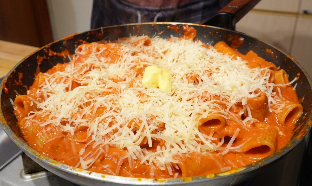 Kostka żółtego masła na wierzchu makaronu z parmezanem na gorącej patelni.