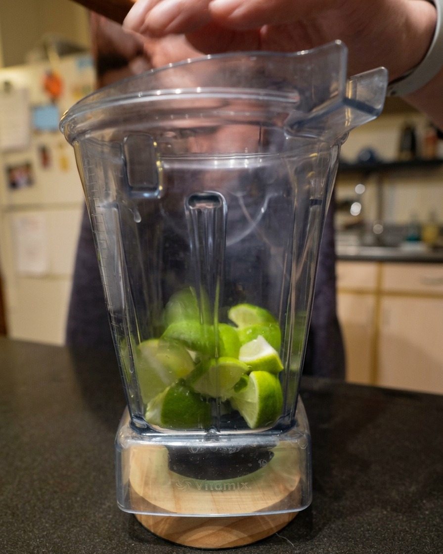 Pokrojone cząstki limonki wewnątrz przezroczystego kielicha blendera.