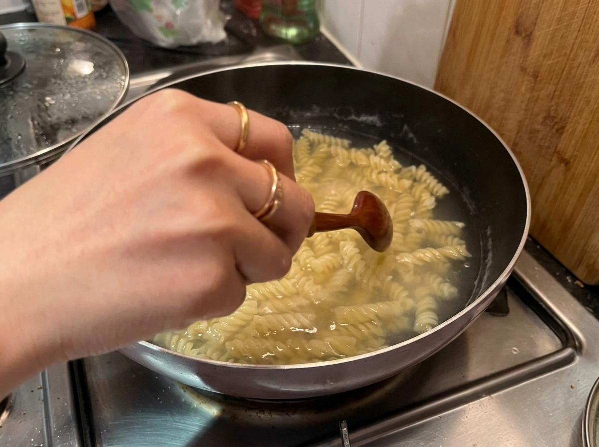 Ręka mieszająca drewnianą łyżką ugotowany makaron fusilli w garnku z gorącą wodą.