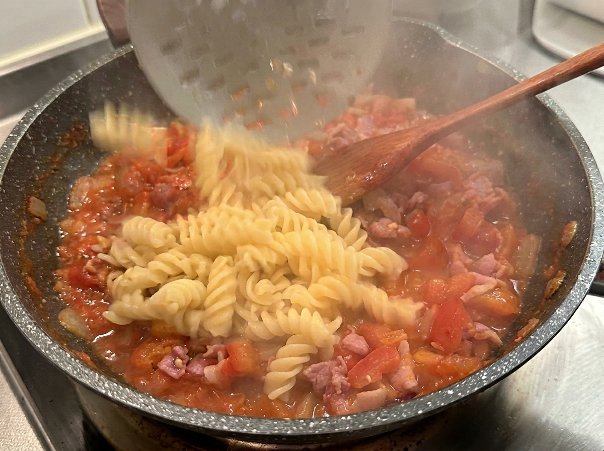 Ugotowany makaron fusilli nakładany łyżką cedzakową do gorącego, czerwonego sosu pomidorowego.