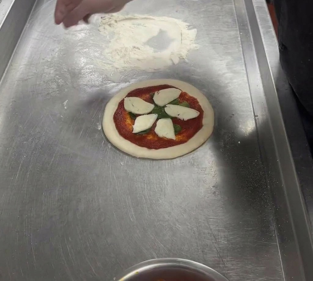 Plastry świeżej białej mozzarelli ułożone na pizzy, skrapiane oliwą z oliwek.