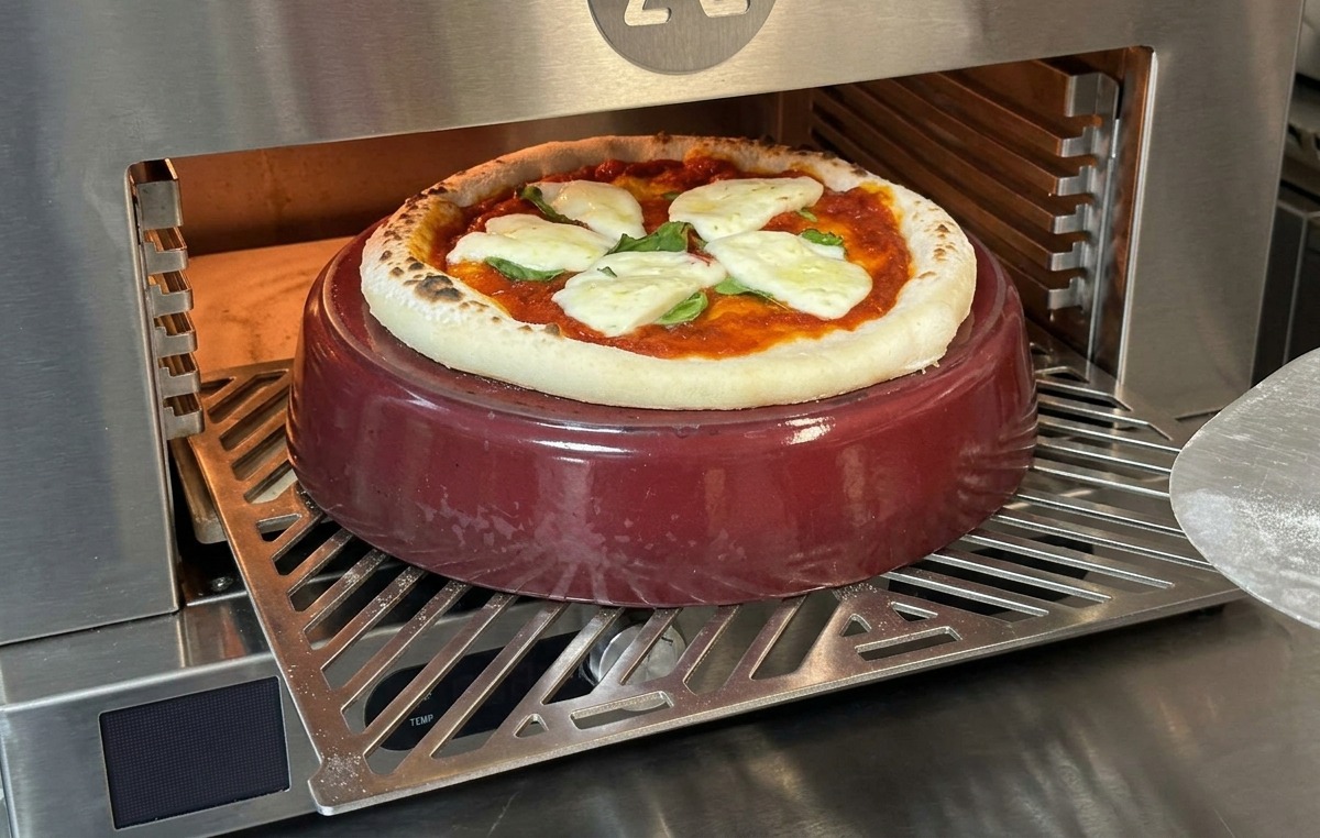 Częściowo upieczona pizza z roztopioną mozzarellą w piecu, z widocznymi rosnącymi brzegami.