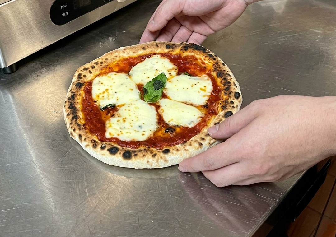 Dłonie trzymające świeżo upieczoną pizzę na blacie, sprawdzające stopień wypieczenia spodu.