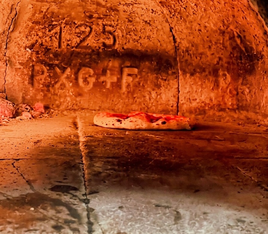 Pizza neapolitańska piekąca się w rozżarzonym piecu, brzegi ciasta wyraźnie rosną i bąblują.