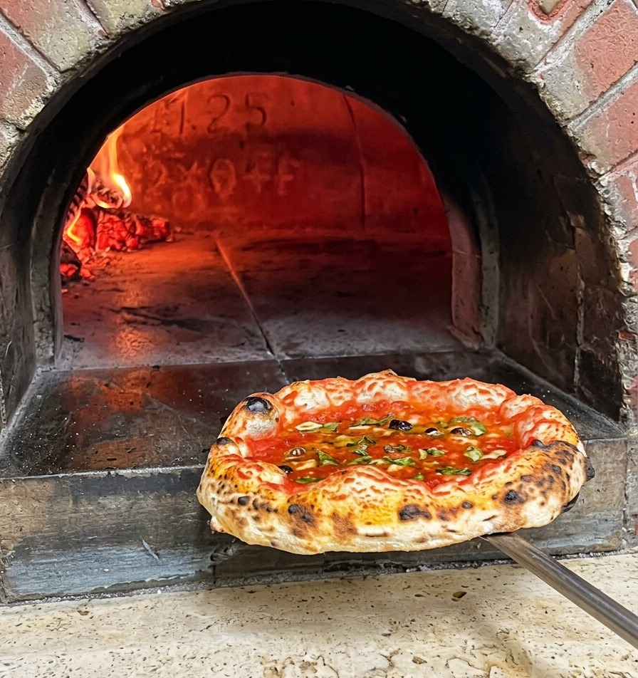 Świeżo upieczona pizza neapolitańska z przypieczonymi brzegami wyjmowana z pieca na metalowej łopacie.