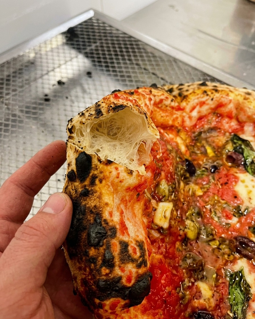 Zbliżenie na kawałek pizzy z naderwanym brzegiem, pokazujące puszyste i napowietrzone wnętrze ciasta.