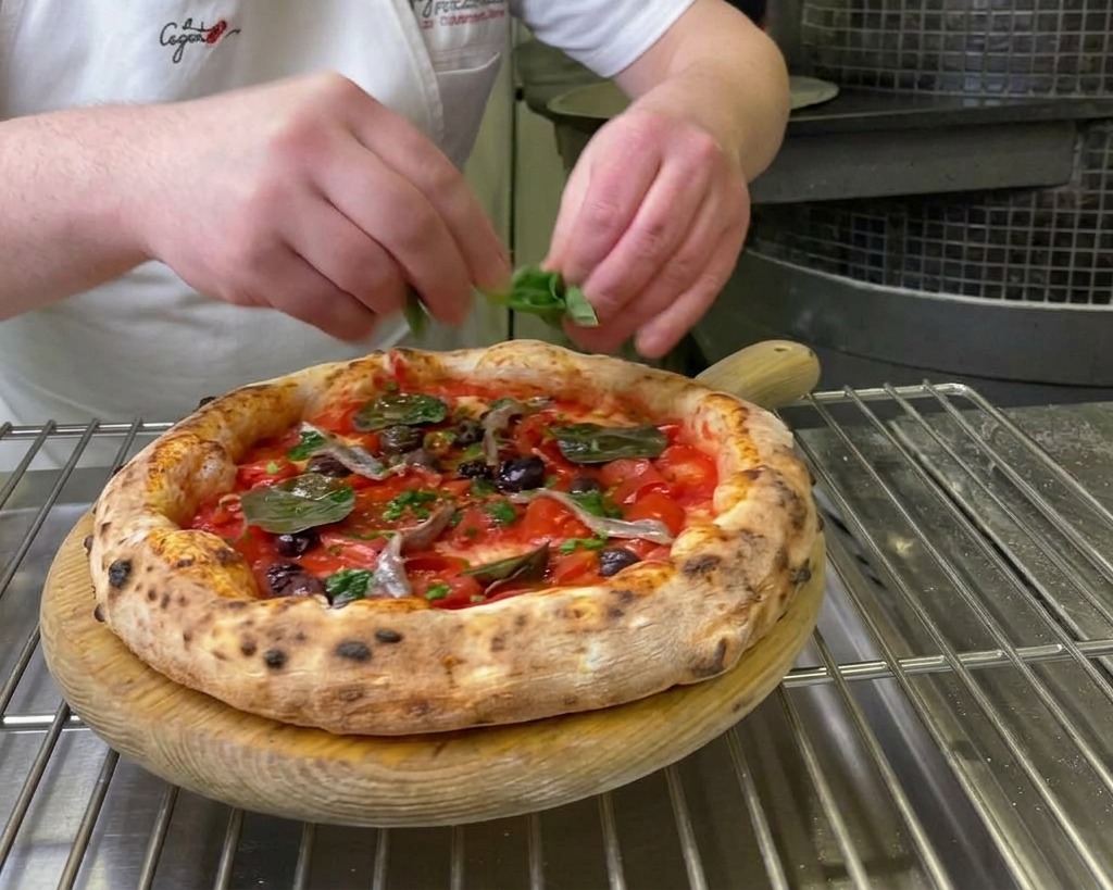 Dłonie szefa kuchni kładące świeże, zielone liście bazylii na świeżo upieczoną pizzę marinara.