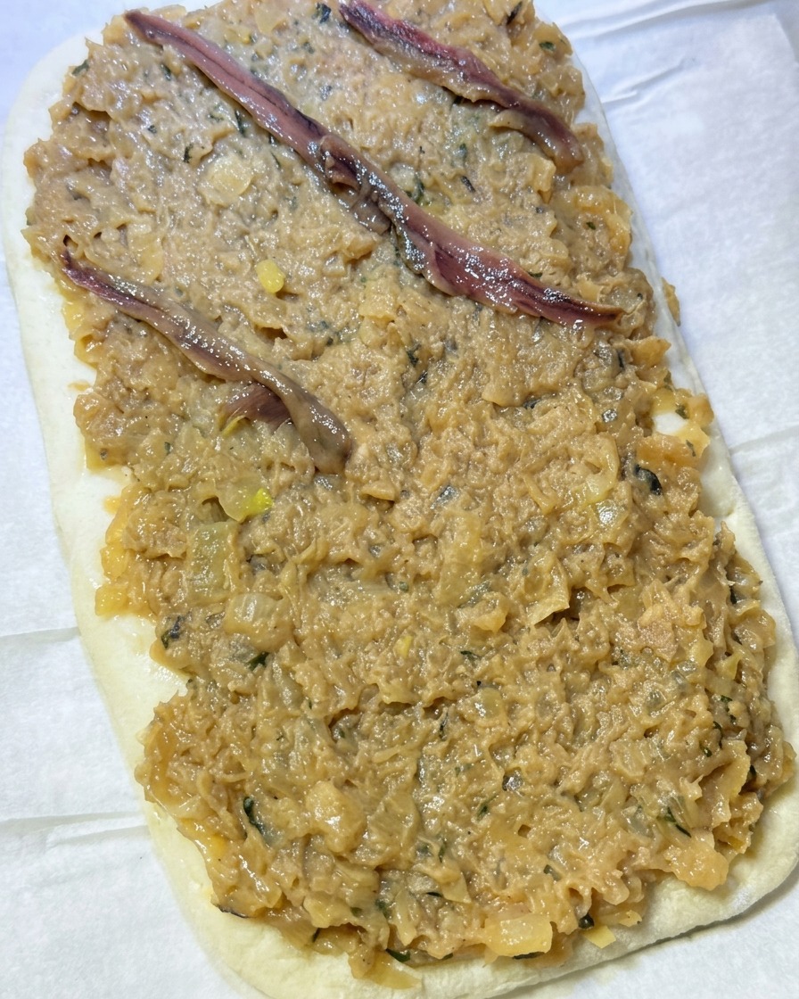 Filety anchois układane w charakterystyczną kratkę na grubej warstwie pasty cebulowej na cieście.