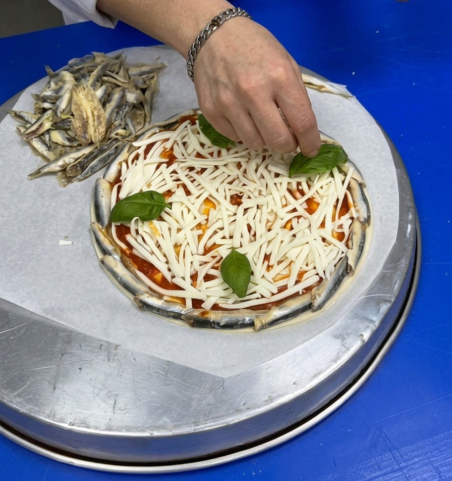 Dłoń układająca całe, świeże liście bazylii na warstwie startego, białego sera na spodzie pizzy.