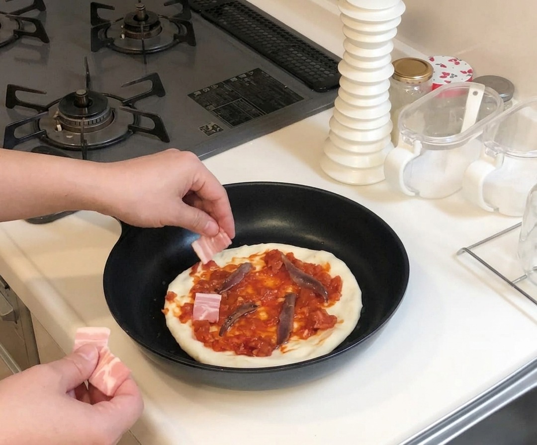 Dłonie kładące małe kawałki surowego boczku na pizzę z sosem i sardelami na patelni.