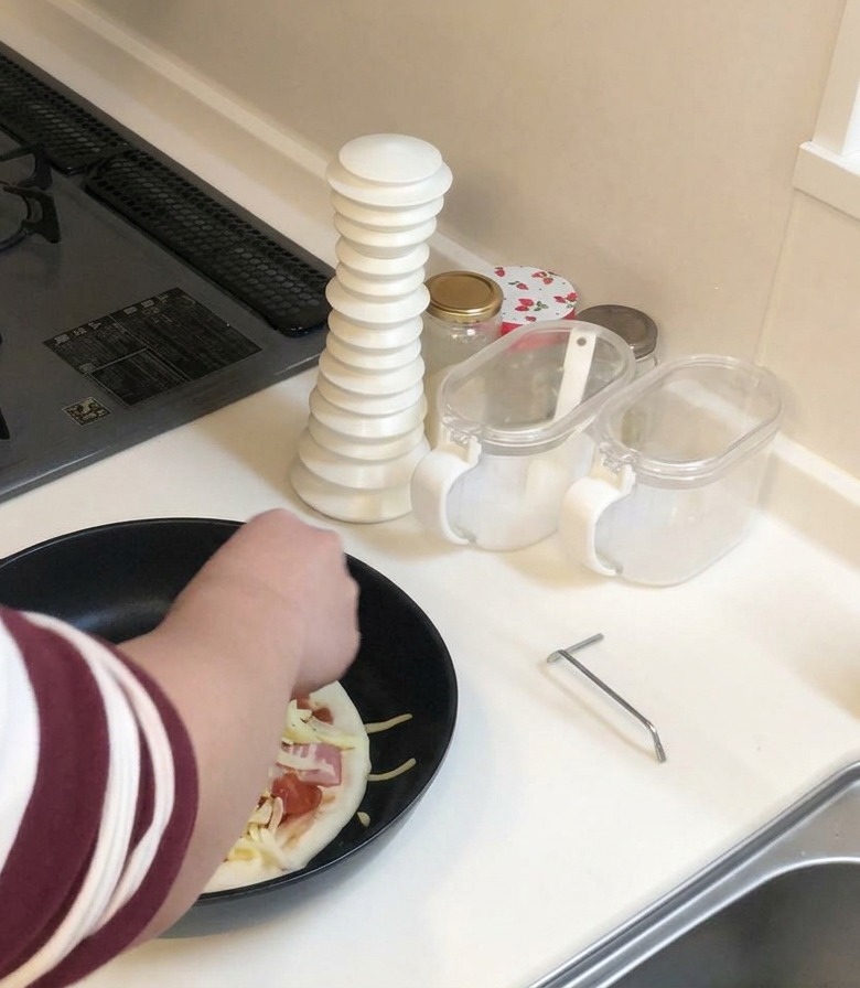 Osoba w koszuli w paski posypująca pizzę na patelni hojną garścią tartego sera.