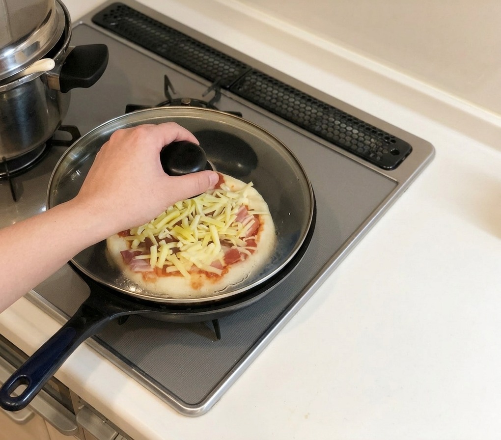 Dłoń nakładająca szklaną pokrywkę na patelnię z pizzą stojącą na kuchence gazowej.