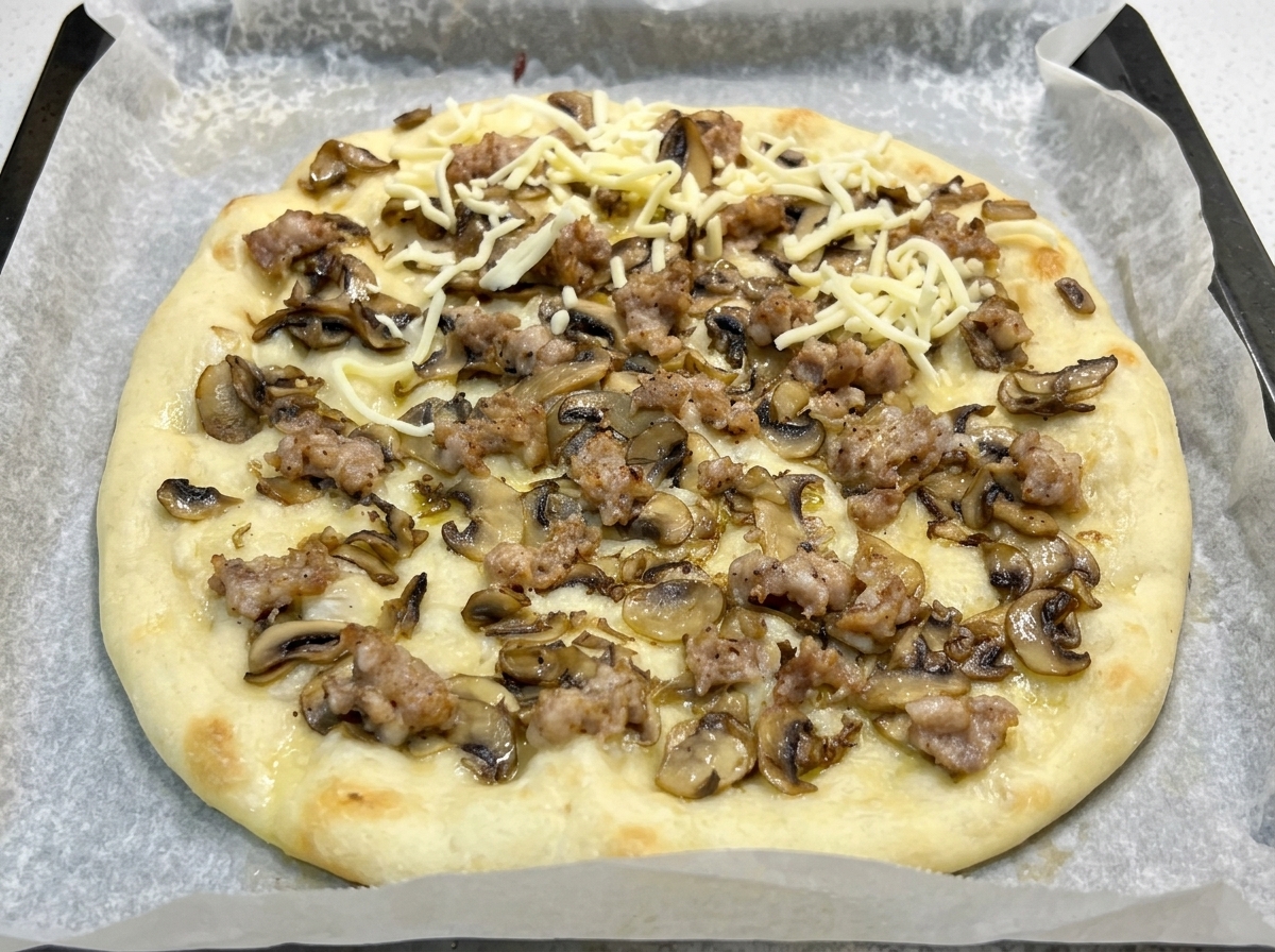 Podpieczony spód pizzy z grzybami i kiełbasą posypany startą mozzarellą.