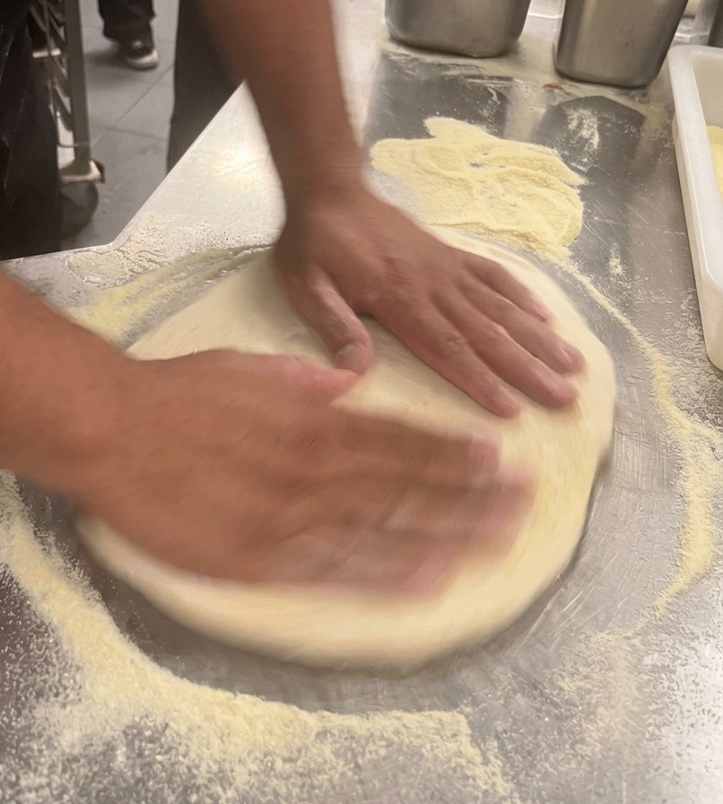 Dłonie szefa kuchni formujące okrągły spód do pizzy na stalowym blacie.