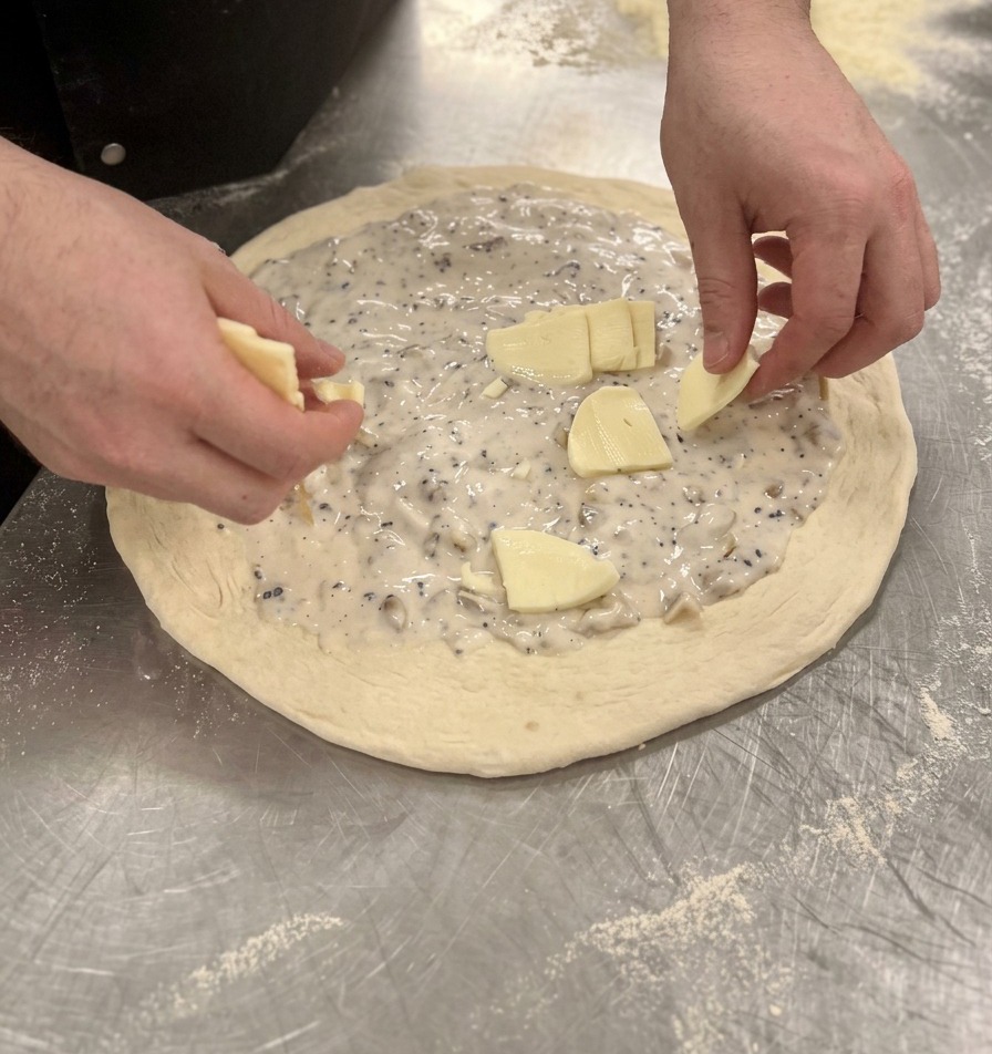 Rozkładanie niewielkich kawałków mozzarelli na białym sosie rozsmarowanym na cieście.