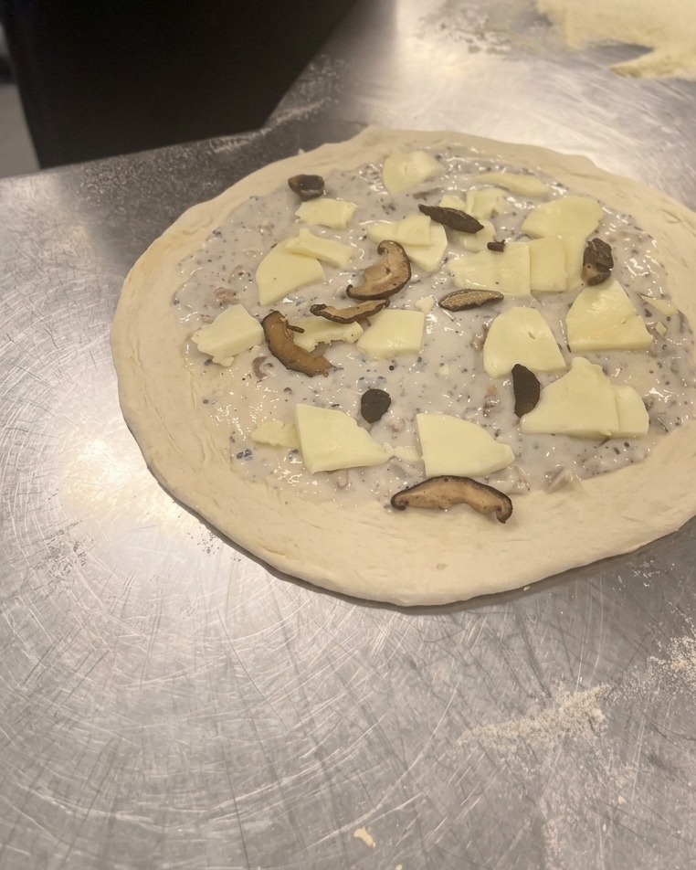 Rozsypywanie podsmażonych plasterków shiitake i pieczarek na ułożonej na placku mozzarelli.