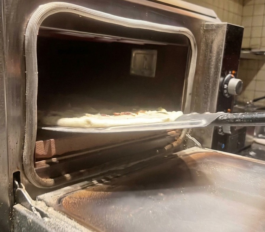 Przenoszenie surowej pizzy do nagrzanego, profesjonalnego pieca za pomocą stalowej łopaty.