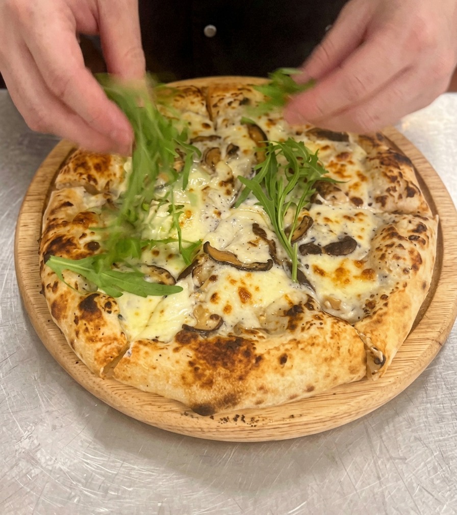 Dekorowanie upieczonej i pokrojonej pizzy listkami zielonej rukoli.