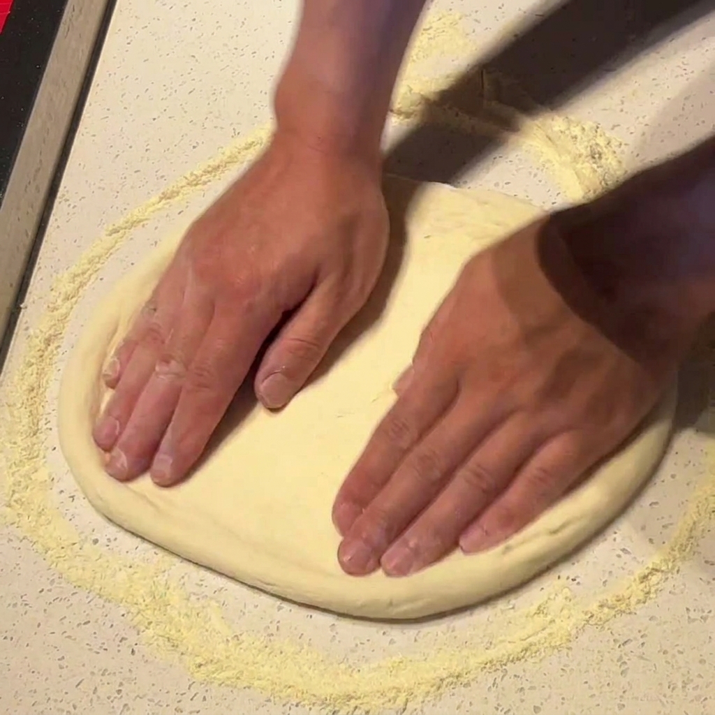 Dłonie dociskające i rozciągające ciasto na pizzę na powierzchni posypanej mąką.