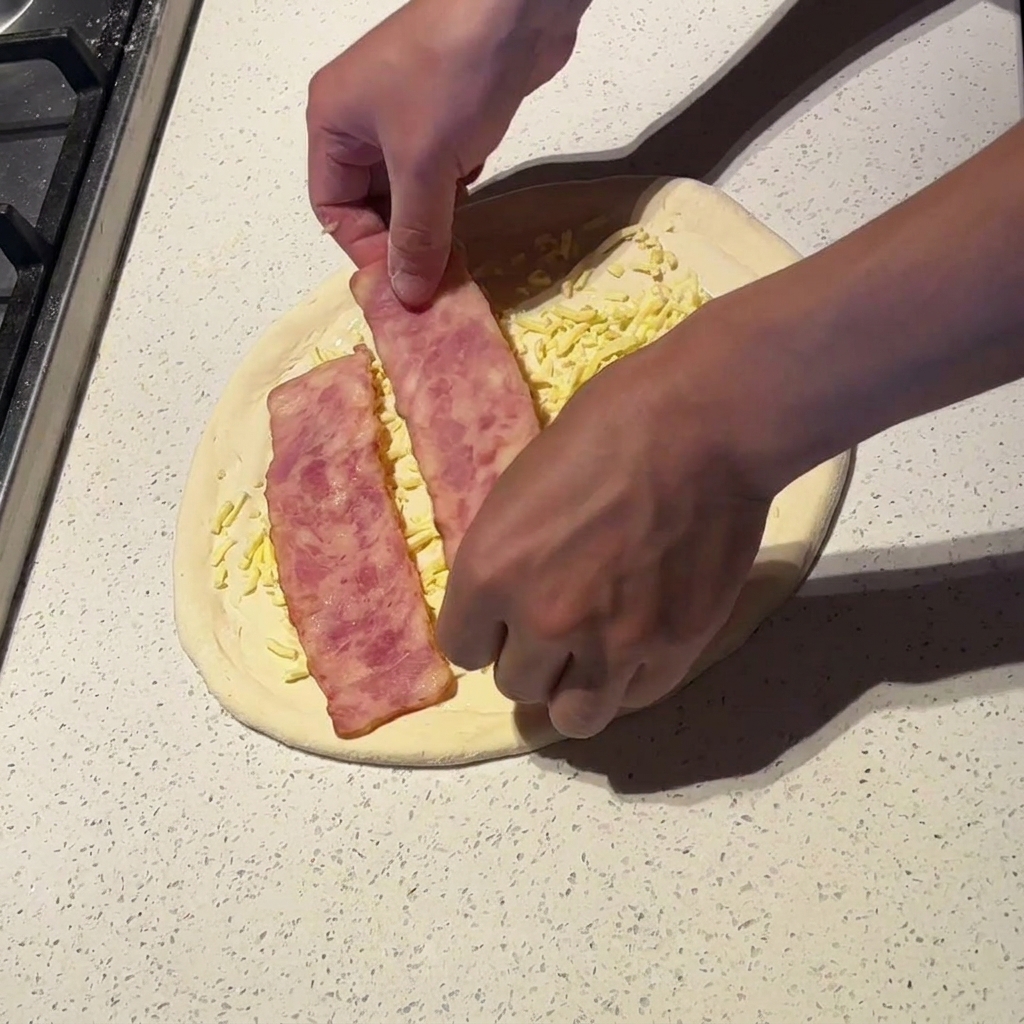 Dłonie układające szerokie plastry lekko podgotowanego boczku na pizzy z sosem i serem.