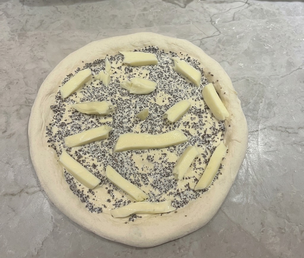 Ciasto na pizzę z sosem truflowym i rozrzuconymi kawałkami mozzarelli.