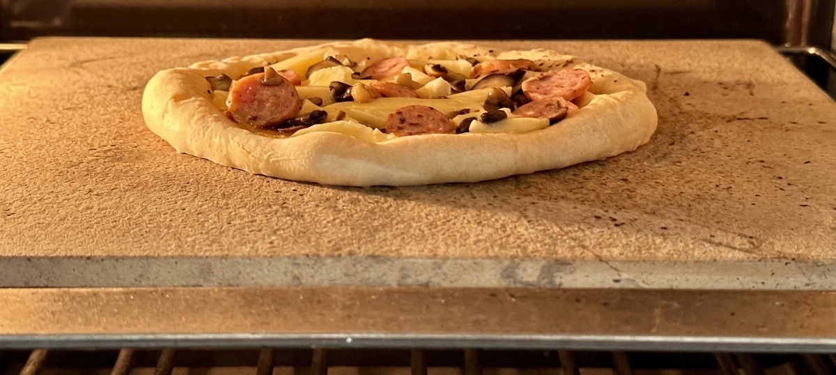 Złożona pizza z kiełbasą i grzybami na kamieniu do pieczenia w gorącym piekarniku.