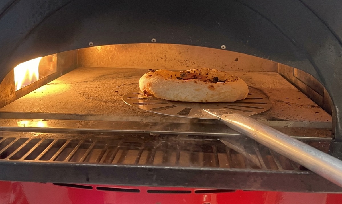 Mała pizza z grzybami i kiełbasą piekąca się w gorącym piekarniku na kamieniu.